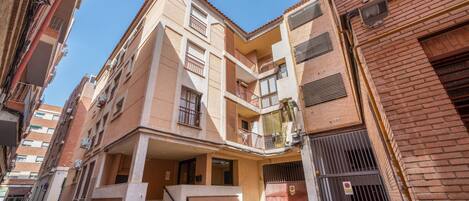 A multi-story residential building with balconies, a gated entrance, and a clear sky.