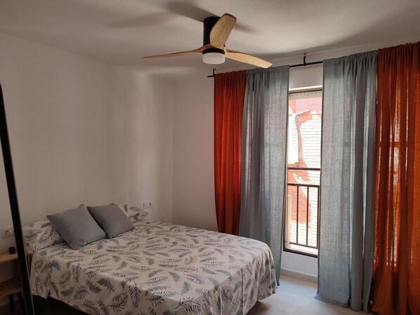 Une chambre à coucher avec un lit, un ventilateur de plafond et une fenêtre avec des rideaux.