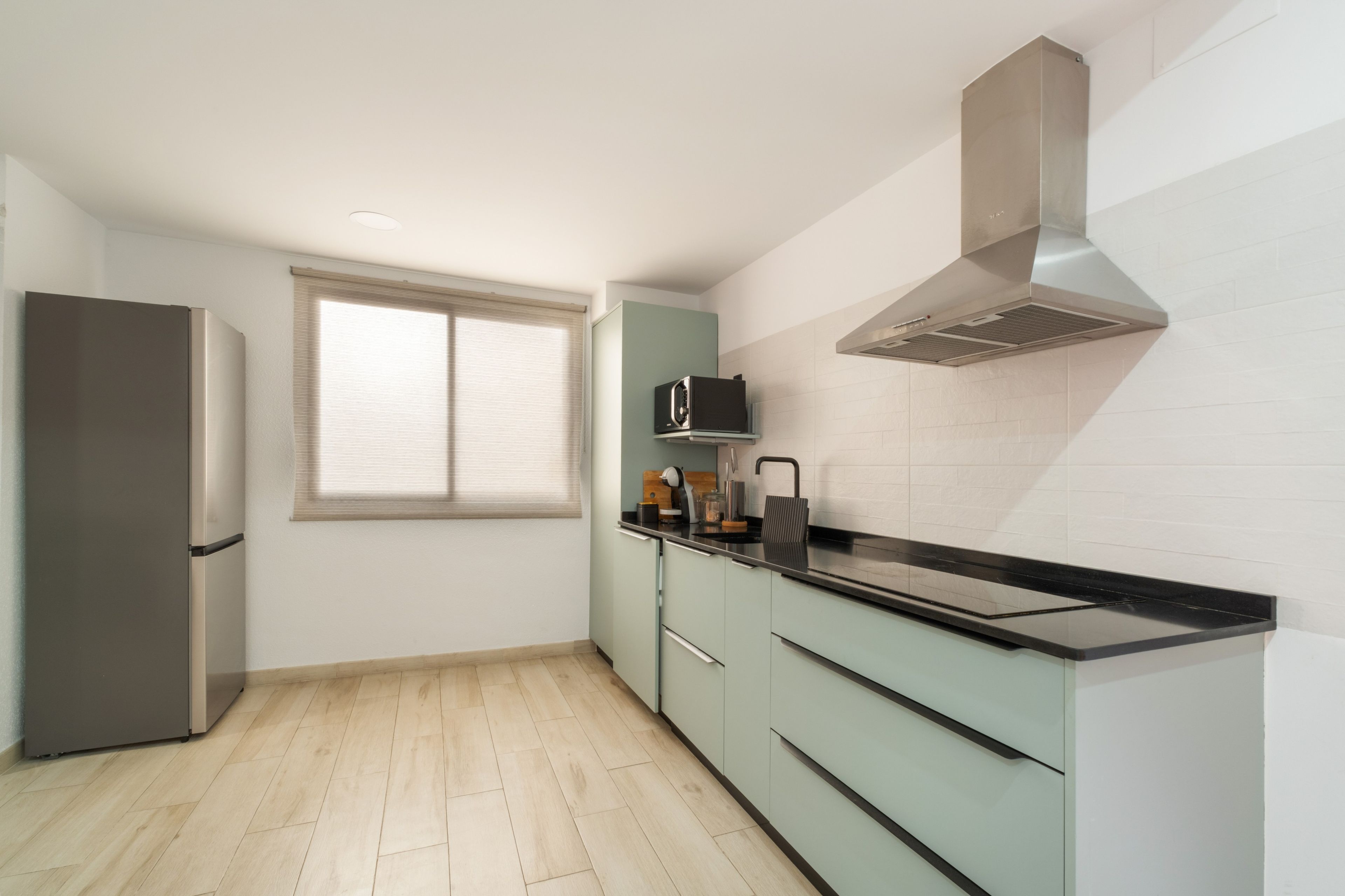Una cocina compacta con microondas integrado, refrigerador de acero inoxidable y encimera negra.