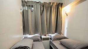 Un alojamiento pequeño, de una sola habitación, con dos camas, una mesita de noche y cortinas.