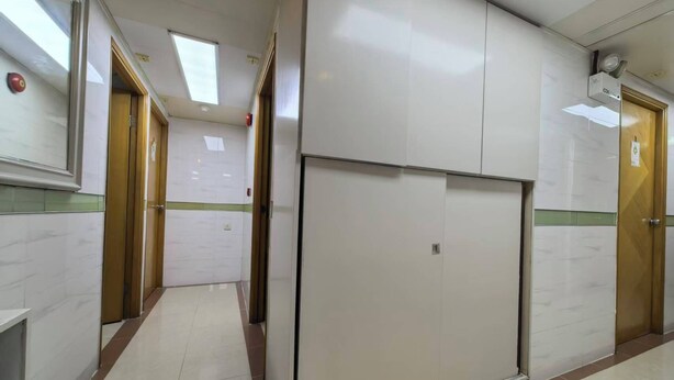 Un pasillo con puertas, un ventilador de techo y suelo de baldosas.