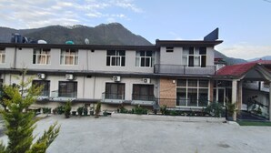 Un edificio de varios pisos con balcones, unidades de aire acondicionado y montañas al fondo.