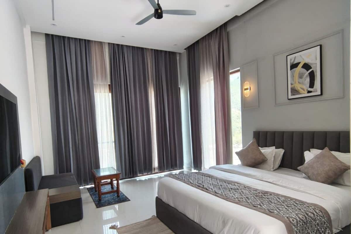 Un dormitorio moderno con una cama grande, un ventilador de techo, un televisor y una ventana con cortinas.