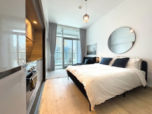 A modern hotel room with a large bed, a round mirror, a city view, and a kitchenette. - Modern Studio in Prime Location & JBR (Dubai Marina)