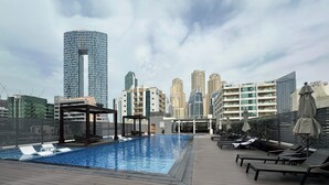 En pool på taget med liggestole, en pergola og udsigt til moderne skyskrabere.