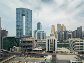 A cityscape with modern high-rise buildings, a prominent curved skyscraper, and a waterfront area with a hotel and parking lot. - Modern Studio in Prime Location & JBR (Dubai Marina)