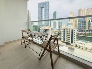 A balcony with a wooden table and chairs, overlooking a cityscape with high-rise buildings and a body of water. - Modern Studio in Prime Location & JBR (Dubai Marina)