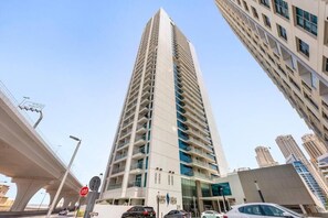 A tall, modern building with multiple floors, a prominent entrance, and a clear sky. - Modern Studio in Prime Location & JBR (Dubai Marina)
