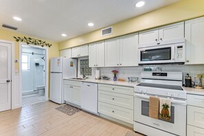 A kitchen with white cabinets, a microwave, a stove, and a refrigerator. - Walk to Cafes! Beachfront Indian Shores Escape (Indian Shores)