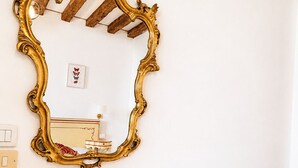 Een kamer met een houten tafel, een witte stoel, een gouden sierlijk spiegelbeeld en een klein fotolijstje aan de muur.