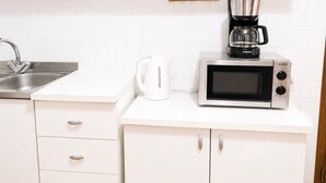 Een keuken met witte kastjes, een roestvrijstalen spoelbak, een waterkoker, een koffiezetapparaat en een magnetron.