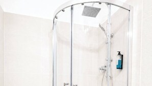 Een douche met glazen wand, een handdouche, een kraan op de muur en een zeepdispenser.