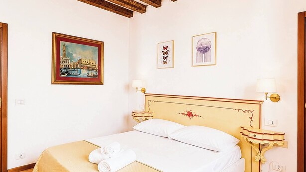 Een slaapkamer met een bed, een houten plafond, een schilderij en een nachtkastje.