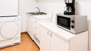 Een kleine keuken met witte kastjes, een ingebouwde magnetron, een koffiezetapparaat en een wasmachine.