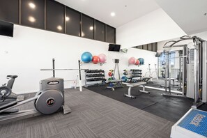 Ein Fitnessraum mit Trainingsgeräten, einem Fernseher und einem Wandregal mit Trainingsbällen.