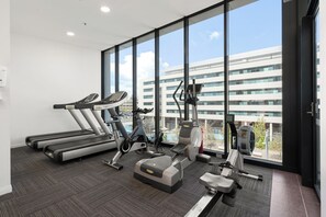 Un gimnàs modern amb cintes de córrer, bicicletes estàtiques i una màquina d'esquí, finestres grans i vista d'un edifici.