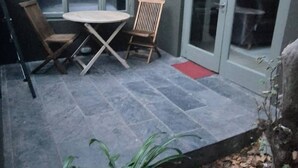 En terrasse med et bord og stole, en skydedør og en lille rød måtte.
