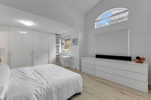 Ein Schlafzimmer mit Bett, Schreibtisch, Kleiderschrank und einem Fenster mit Jalousien.