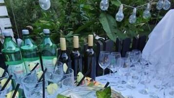 A table with a large mason jar filled with a beverage, surrounded by glasses and bottles, with a plate of fruit and a white tablecloth.
