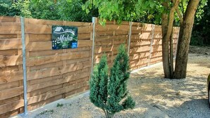 Ein Holzzaun mit einem Schild, einem kleinen Baum und einem Kiesweg.