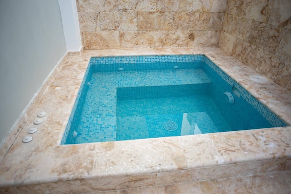 A rectangular hot tub with a tiled interior, surrounded by marble walls.