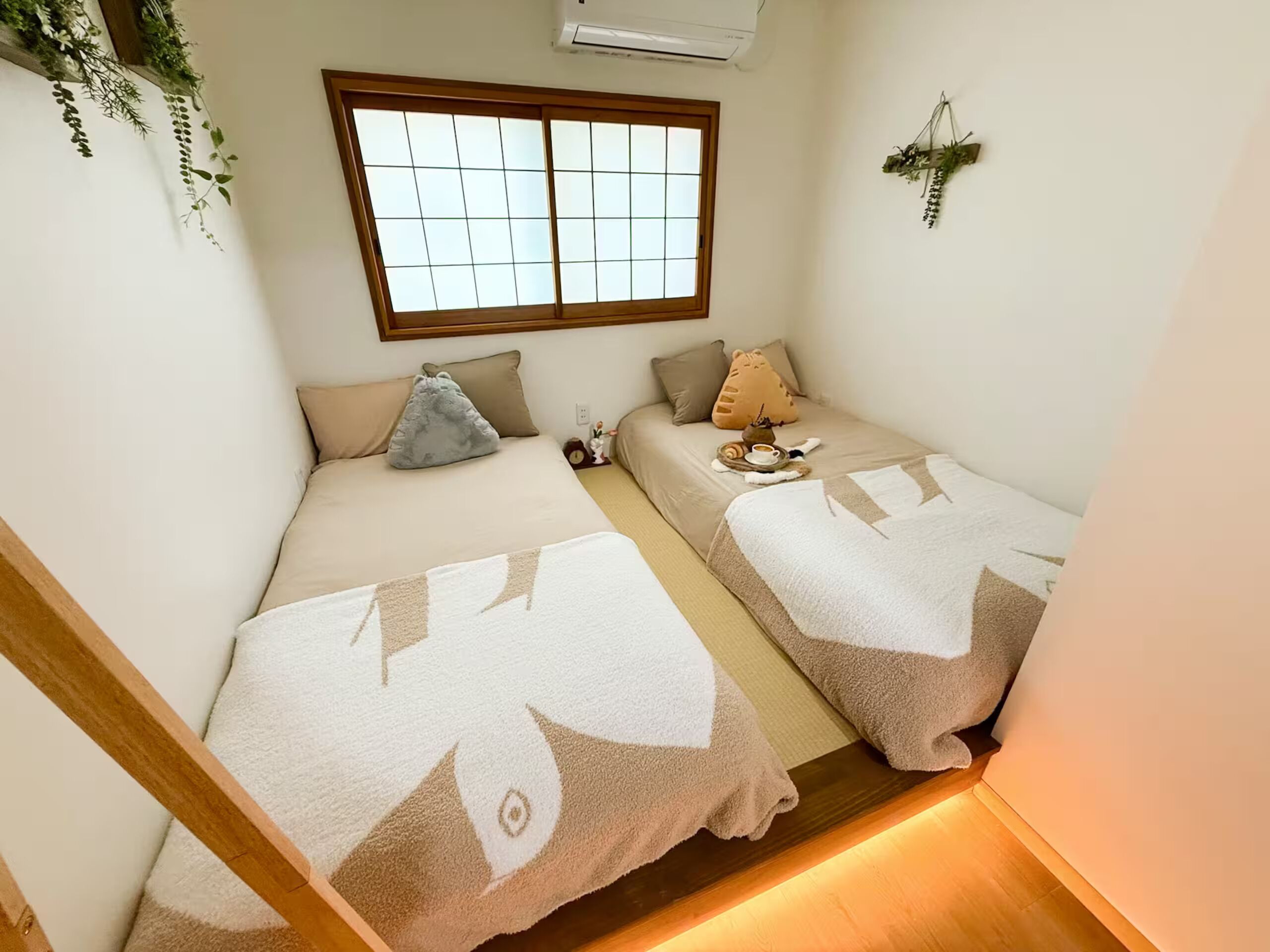Una habitación con dos camas, una ventana y una mesita con una taza y un libro.