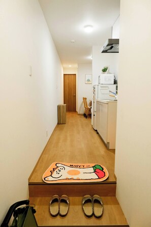 Ein Flur, der zu einer Küche mit Holzboden, einer Fußmatte mit Katzenmotiv und einem Schuhpaar auf den Stufen führt.