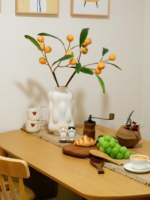 Ein Holztisch mit einer weißen Vase, Keramikfiguren, einem Holzlöffel, einem Holzbrett mit Trauben, einem Holzcroissant, einer Kaffeetasse und einem Honigdipfer.