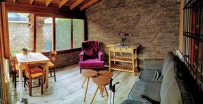 Una habitación acogedora con una pared de piedra, un sillón morado, una mesa de madera con sillas y un sofá.