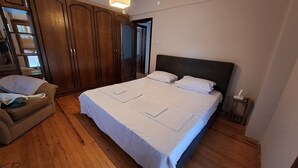 A bedroom with a large bed, wooden wardrobe, and a bedside table.
