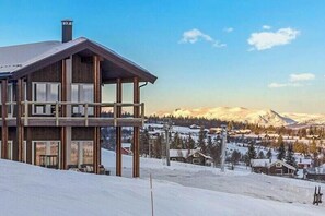 Un edifici de fusta de diversos pisos amb un balcó, davant d'un paisatge nevós amb muntanyes al fons.