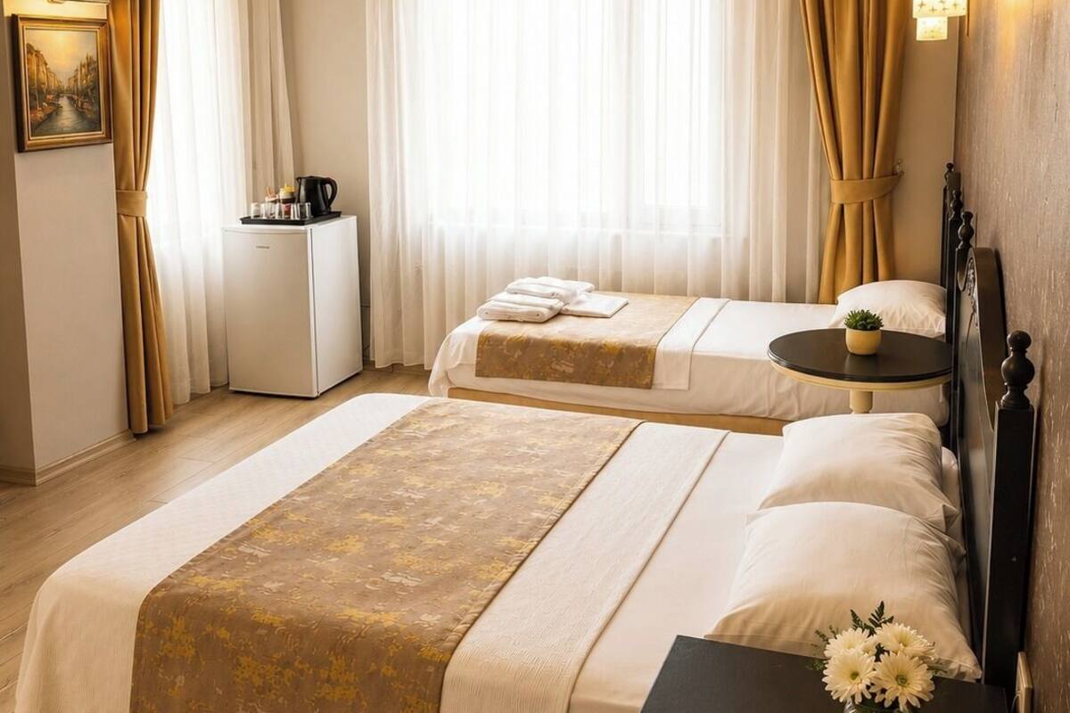 Habitación de hotel con dos camas, una mesita de noche con teléfono, una pequeña mesa con lámpara y un cuadro en la pared.