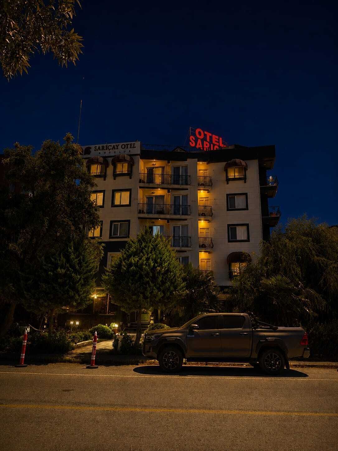 Un edificio de varios pisos con balcones, un letrero que dice 'SARICAY OTEL' y un vehículo estacionado al frente.
