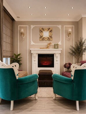 Una sala de estar con chimenea, dos sillones color turquesa, un espejo decorativo e apliques de pared.