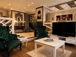 Una sala de estar con un sillón verde, una mesa de centro blanca, un televisor y una escalera que sube a otro nivel.