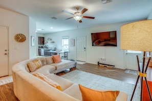 A living room with a sectional sofa, a ceiling fan, a dining area, and a kitchen in the background. - South Austin Hub Near Airport & McKinney Falls! (Austin)