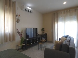 Una sala de estar con un televisor de pantalla plana, un sofá, una mesita y una planta en maceta.