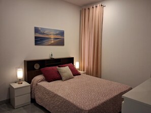 Een slaapkamer met een bed, nachtkastjes, een lamp, een schilderij en een gordijn.