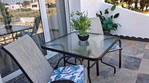 Een tafel met glazen blad en stoelen op een balkon, een plant in pot en uitzicht op gebouwen.