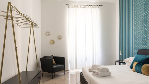 Une chambre d’hôtel avec un lit, une chaise, une commode et un étendoir à linge en métal.