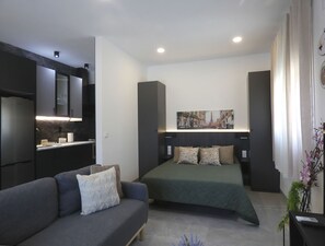 A modern bedroom with a bed, a sofa, a kitchen area, and a cityscape painting on the wall. - Estación 102 Complete loft apartment. (Peñiscola)
