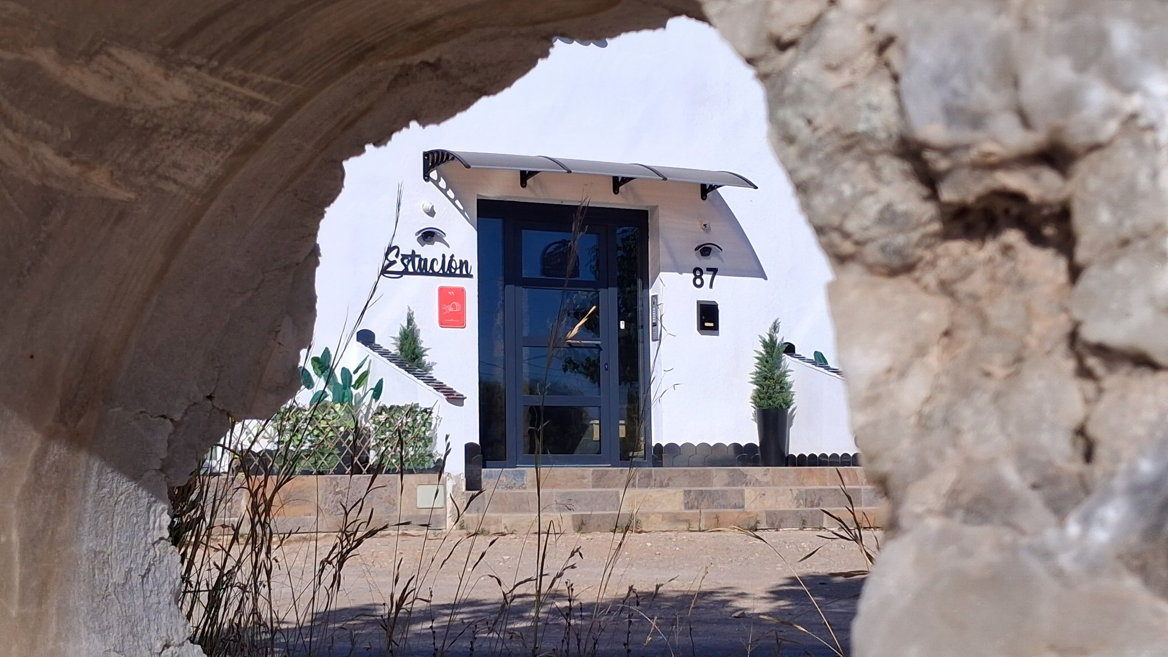 A building with a blue door, a sign reading 'Estacion', and the number '87' above the door.