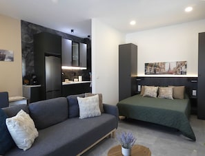 A modern, compact living space with a sofa, a bed, a small kitchen area, and a dining table.