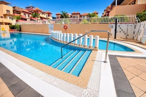 Una piscina con barandilla de seguridad, solárium con baldosas y un flotador salvavidas.