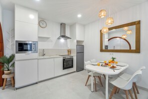 A modern kitchen with white cabinets, a stainless steel microwave, a built-in oven, and a dining area with a white table and chairs. - Charming Apartment in Arona Comfort and Convenience Await (Arona)