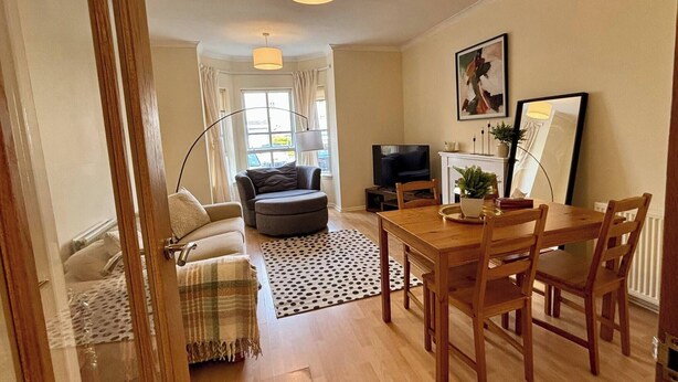 A living room with a sofa, ottoman, dining table, chairs, a TV, and a fireplace. - City Centre Home - Away from Home (Edinburgh)