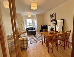 A living room with a sofa, ottoman, dining table, chairs, a TV, and a fireplace.
