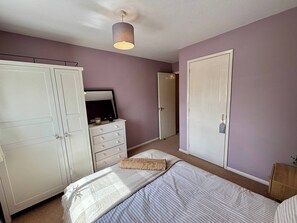 Un dormitorio con cama, cómoda, armario, una puerta y una lámpara en el techo.