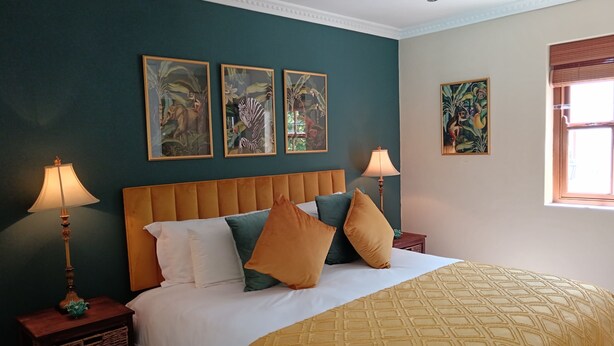 Ein Schlafzimmer mit einem Bett, zwei Nachttischen, Wandbildern und einem Fenster.