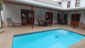 Ein Schwimmbecken mit Fliesenbord, Holzstühlen und einem Tisch.